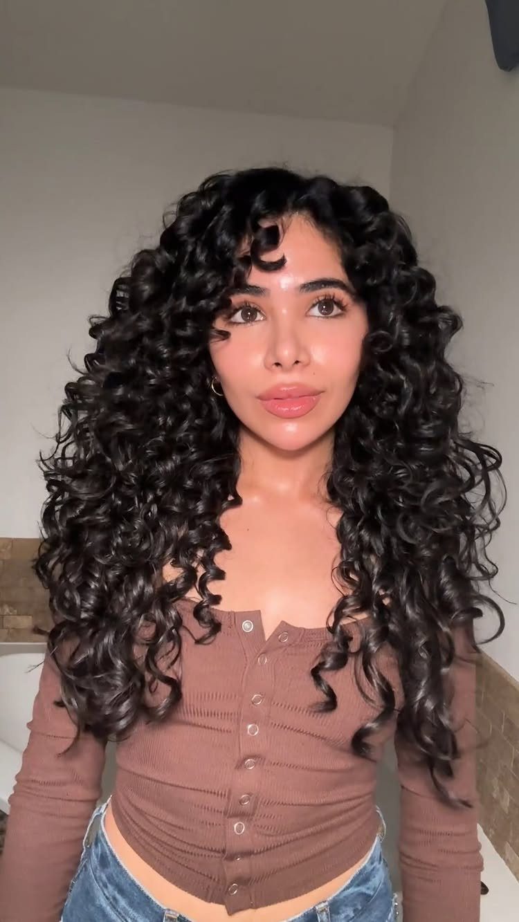 Woman with long, dark, defined curly hair and bangs