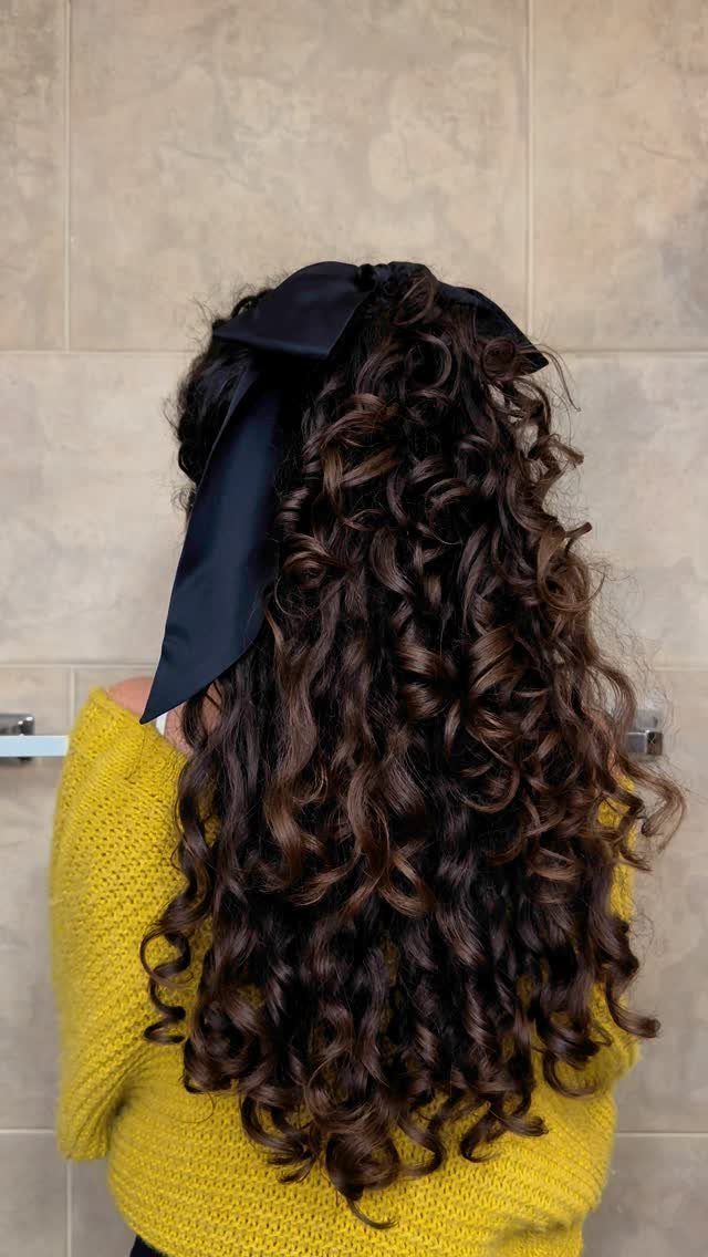 Long dark curls fall over a yellow sweater beneath a wide black hair accessory