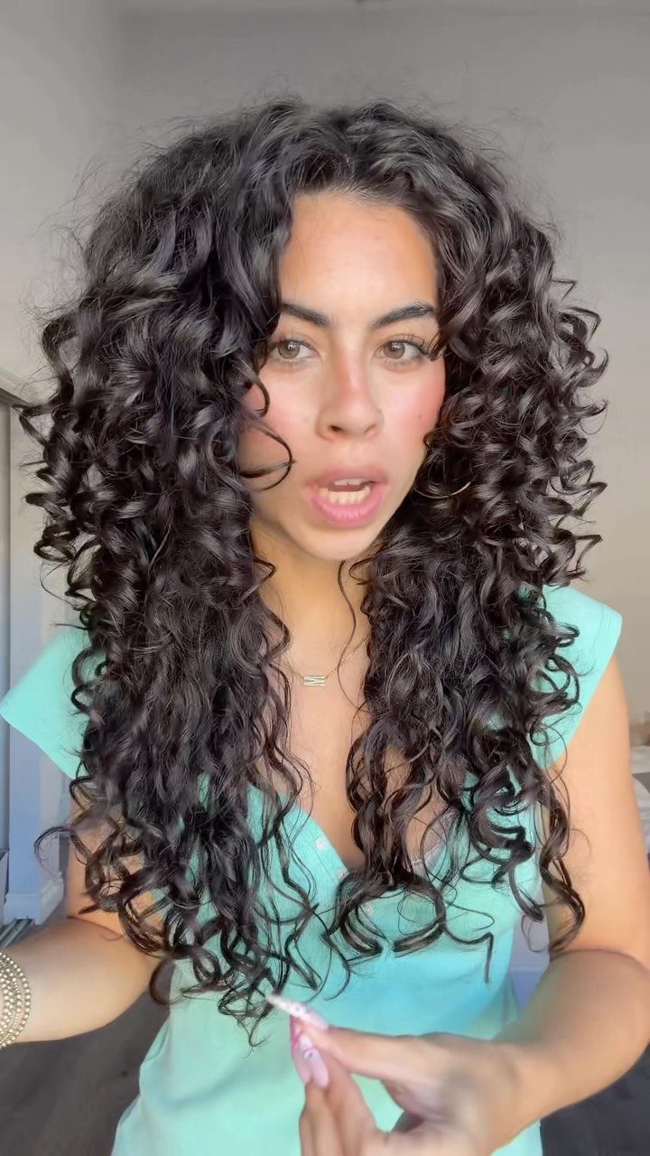 Woman with long, dark, defined curls wearing a turquoise top indoors