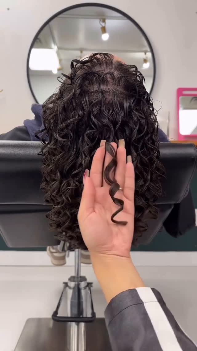 Dark curly hair with a hand displaying one defined spiral curl in a salon