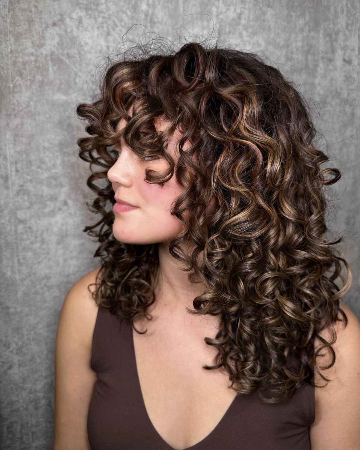 Woman with shoulder-length dark curls accented by subtle caramel highlights
