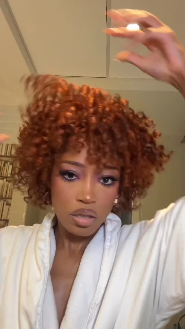 Woman with shiny copper-red curls poses in a white robe indoors