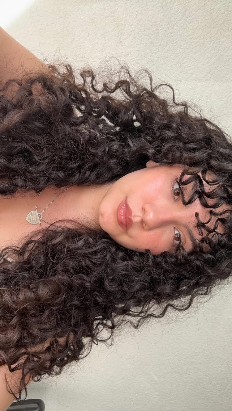 Person with long dark curls and a curly fringe framing the face