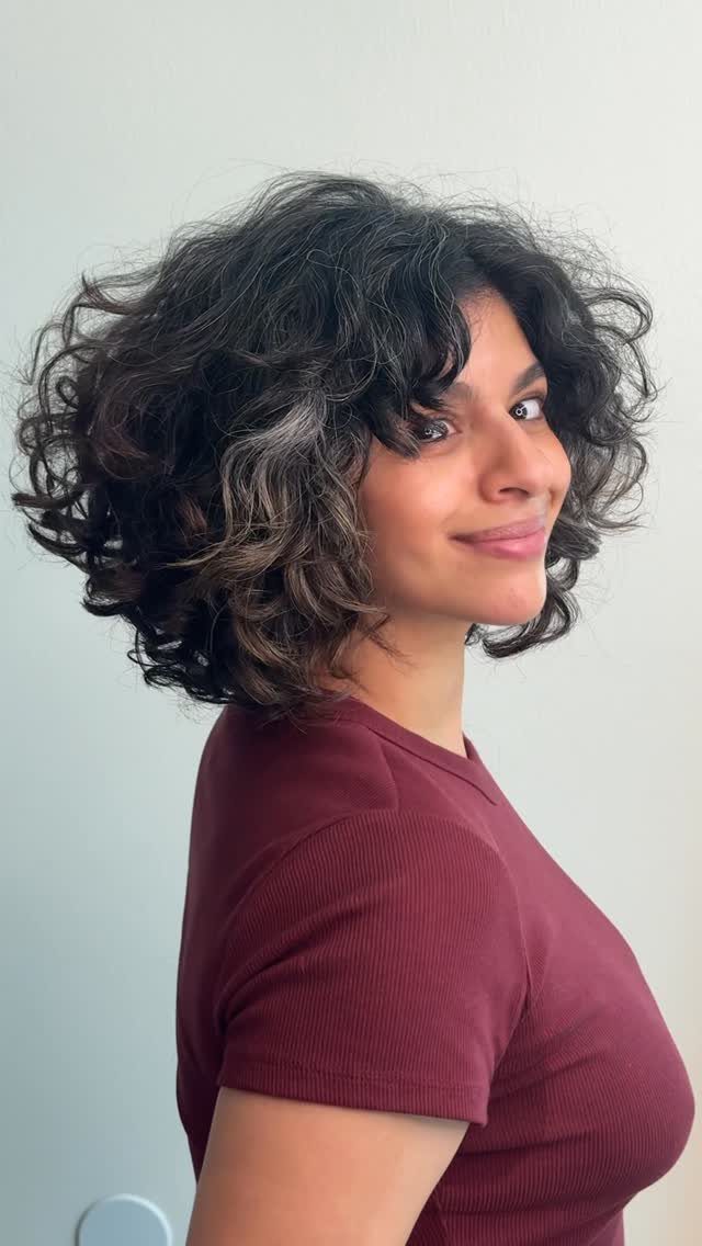 Woman showing a voluminous chin-length dark curly bob with subtle highlights