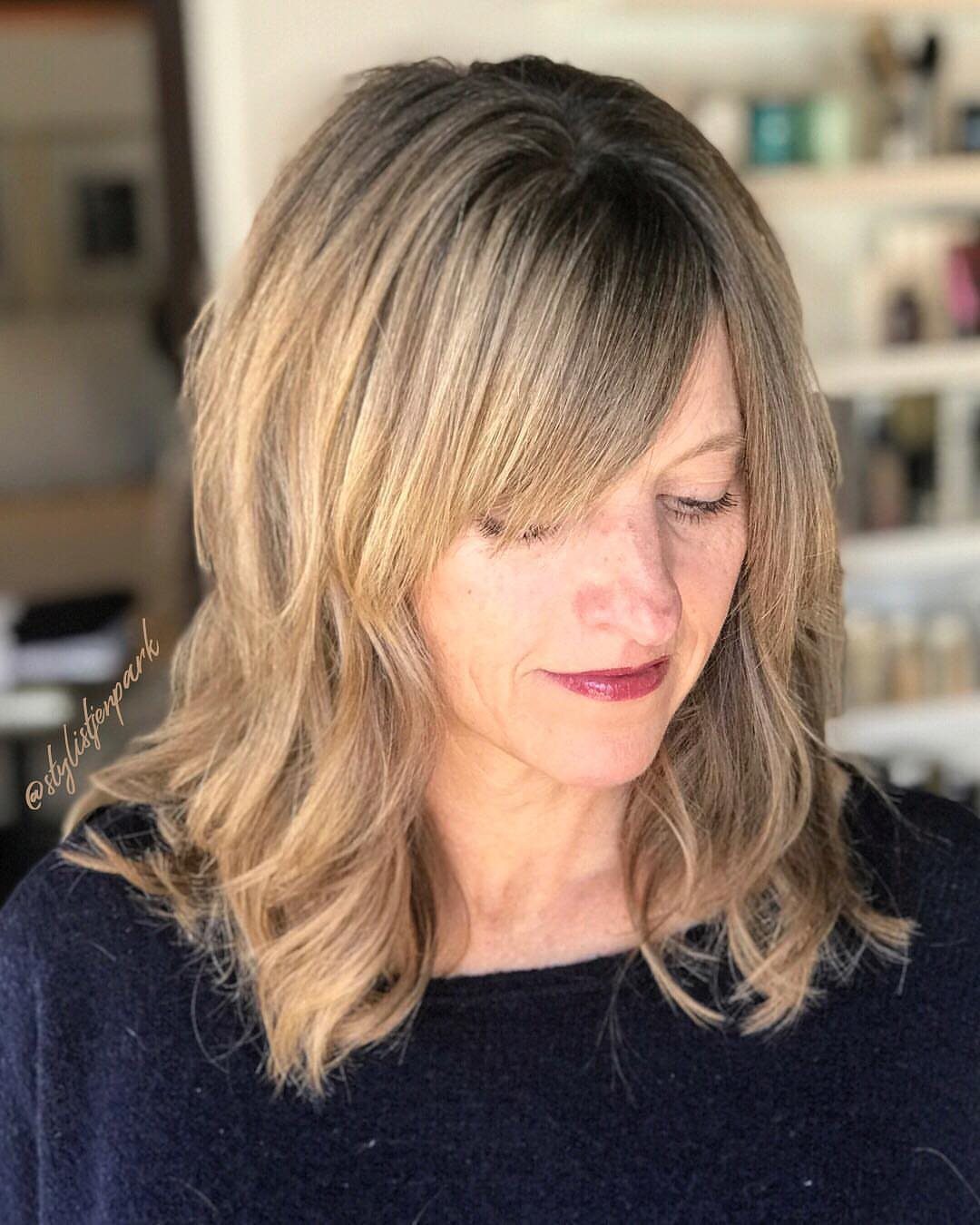 Woman with shoulder-length blonde waves and long side-swept bangs