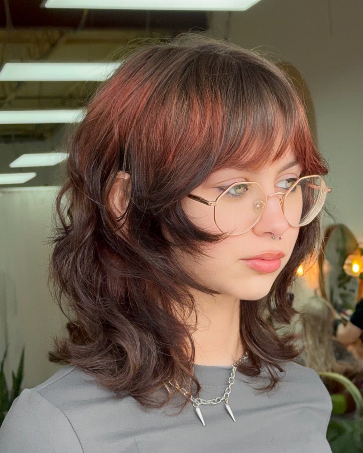 Woman with wavy layered hair and piecey bangs wearing round glasses