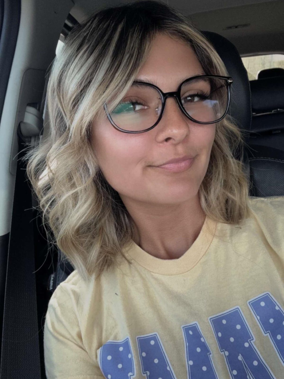 Woman with highlighted shoulder-length waves and face-framing bangs taking a car selfie