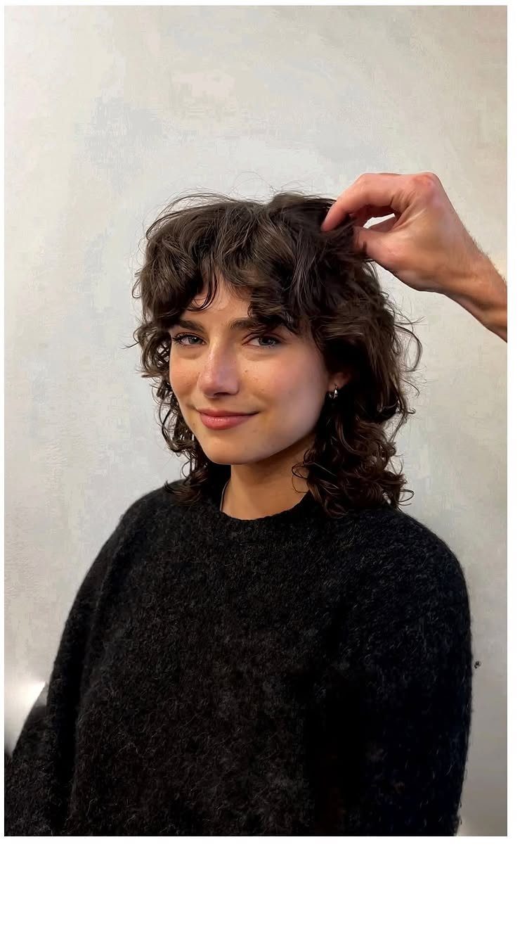 Woman with dark shoulder-length waves and a dense fringe in a black sweater
