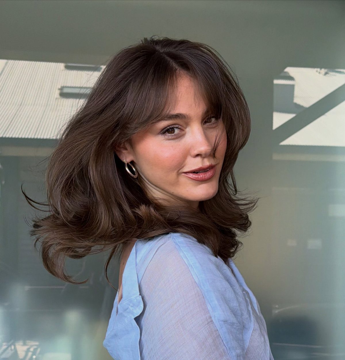Woman showing wispy bangs blended into shoulder-length dark wavy hair