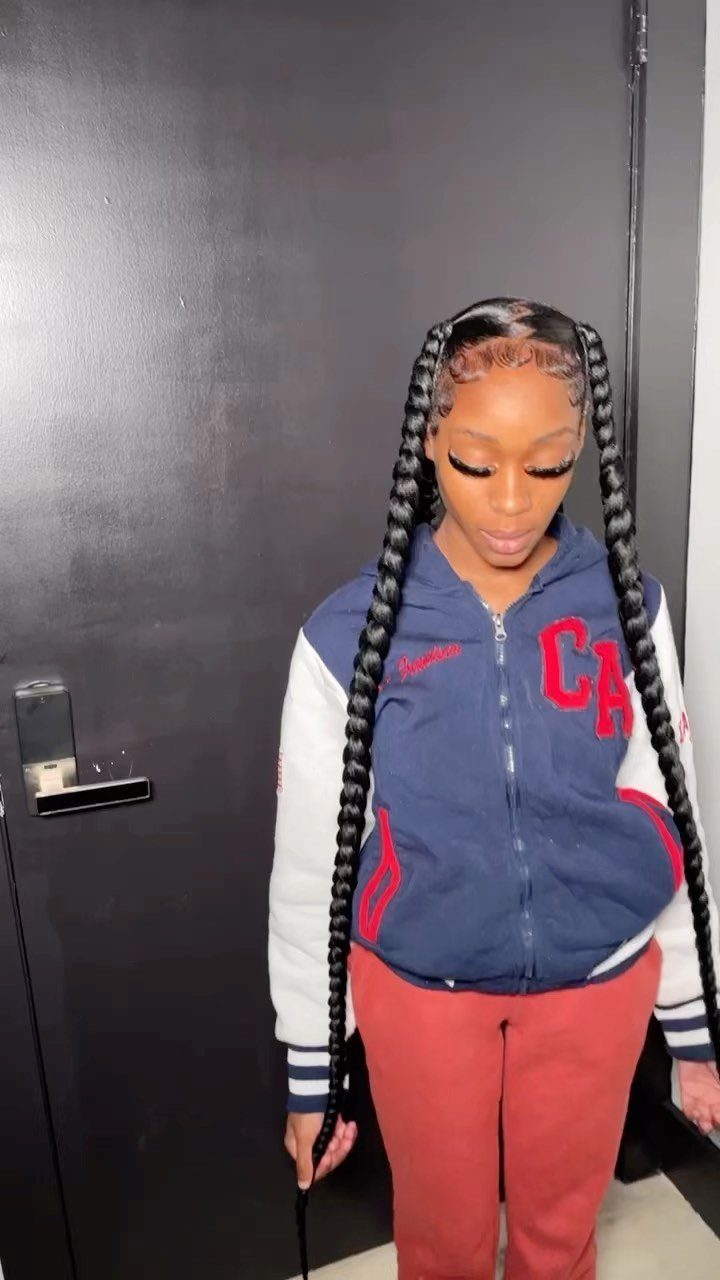 Woman wearing two long black braided pigtails against a dark door