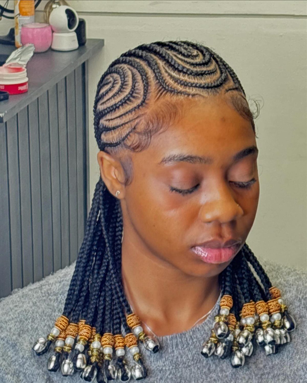Long black braids with gold and silver beads frame a detailed cornrow hairstyle