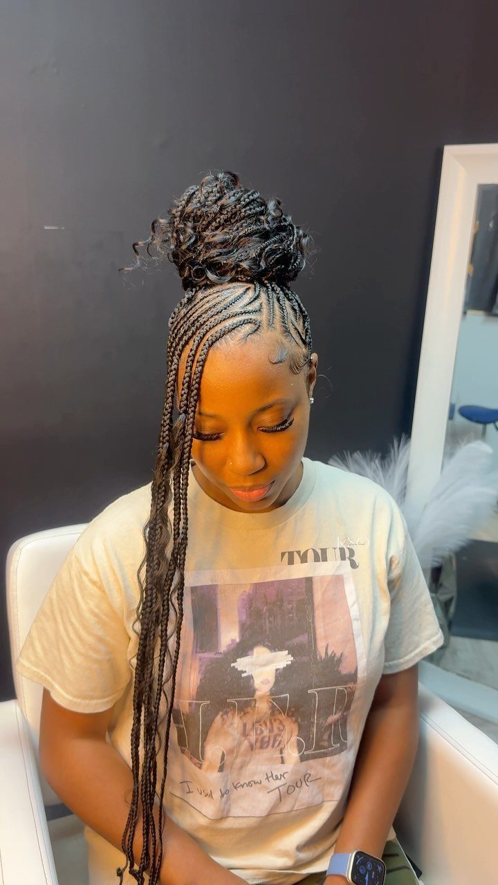 Intricate cornrows flow into long braids and a high bun on a seated person