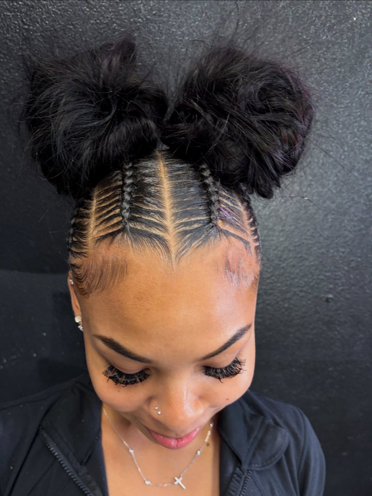 Black cornrows sweep into two fluffy space buns atop the head