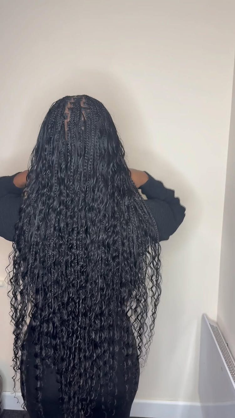 Long black box braids with loose wavy ends fall down a person's back