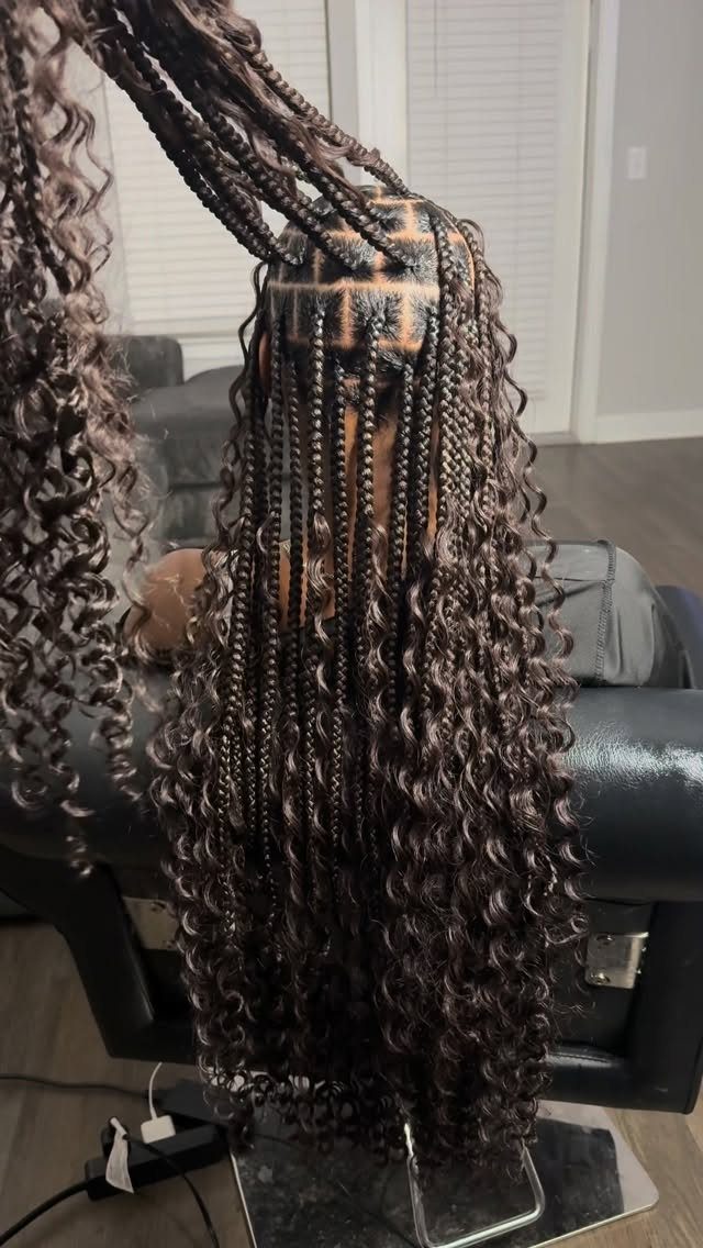 Long dark box braids with curly ends are lifted to reveal geometric scalp sections.