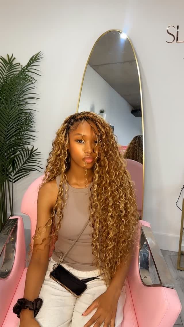 Woman with long honey-blonde side-part braids and loose curls in a salon