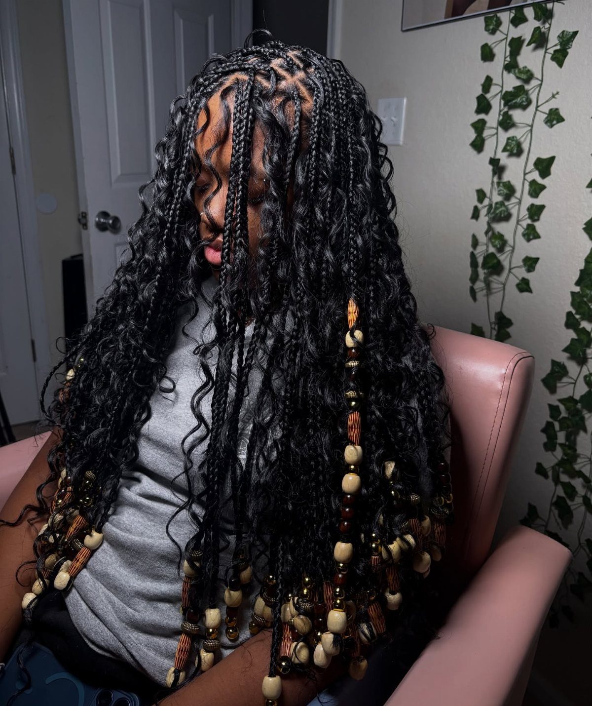 Long black braids with loose curls and tan beads drape over a seated person