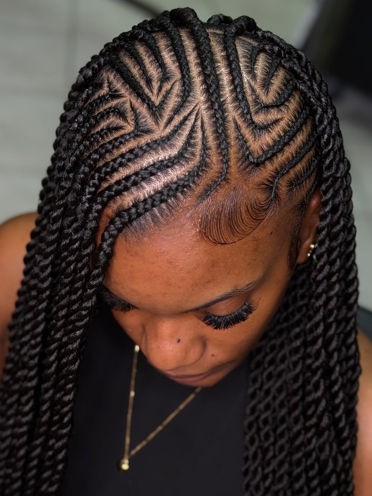 Curved snaky cornrows feed into long black braids over the scalp