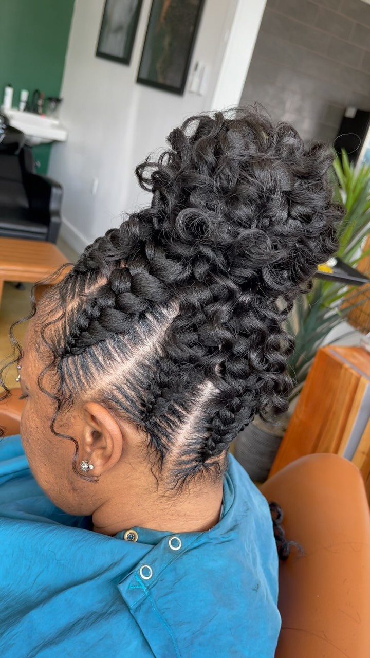 Curly braided bun with neat side braids on a person wearing a blue salon cape