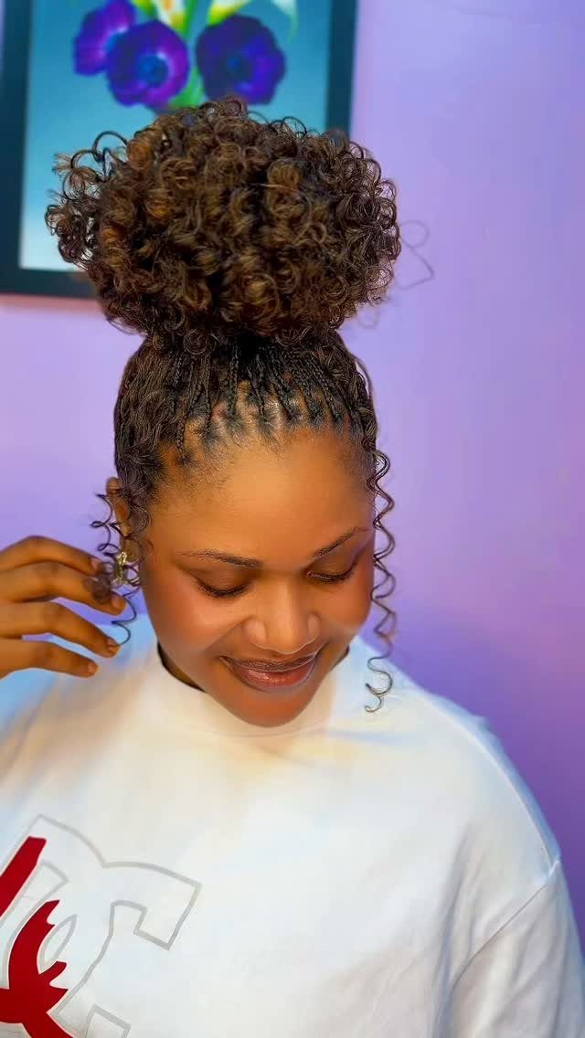 Curly high bun gathered above neat scalp braids, with loose tendrils framing her face