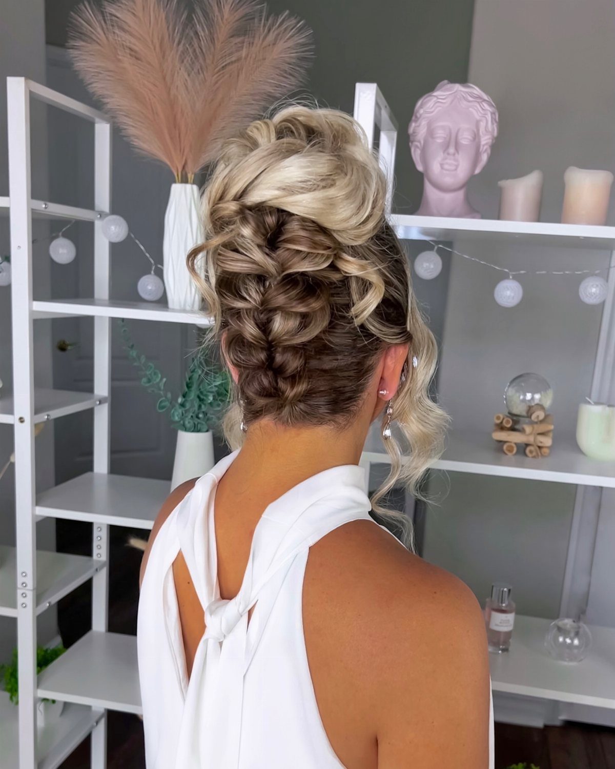 Woman showing an intricate high braided bun with loose curls indoors