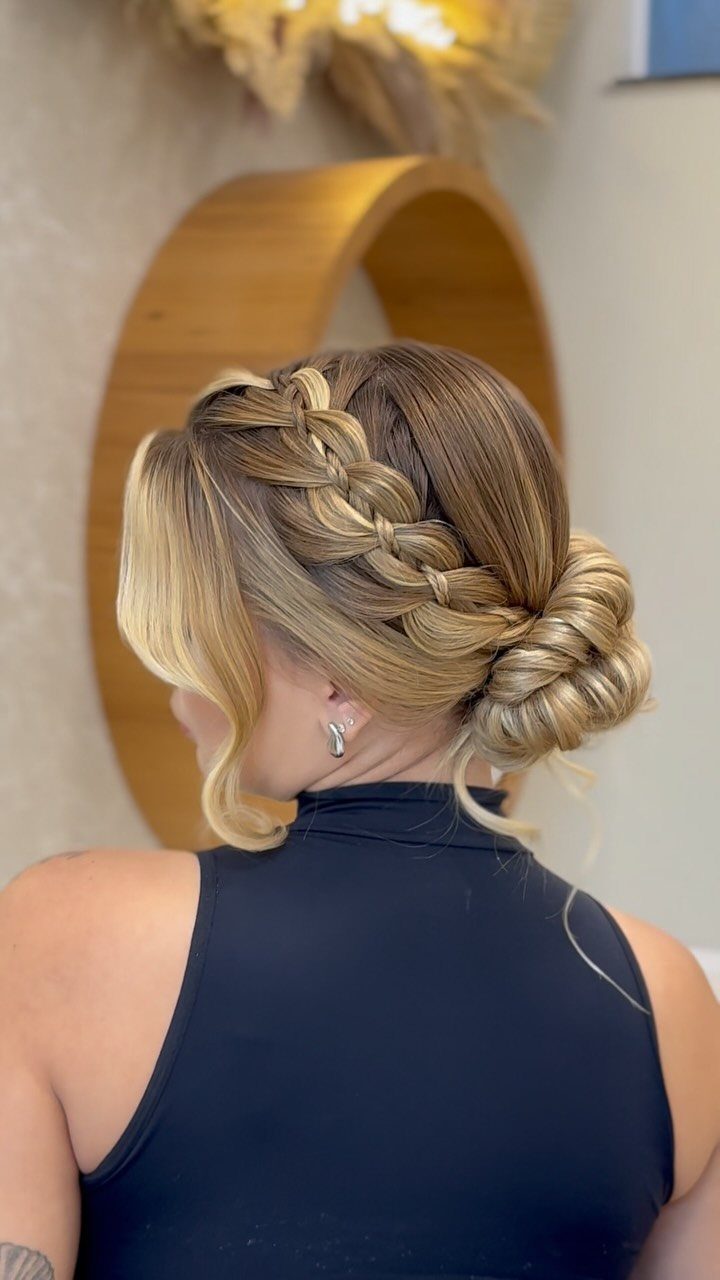 Side braid wraps into a full low bun on a woman's blonde hair