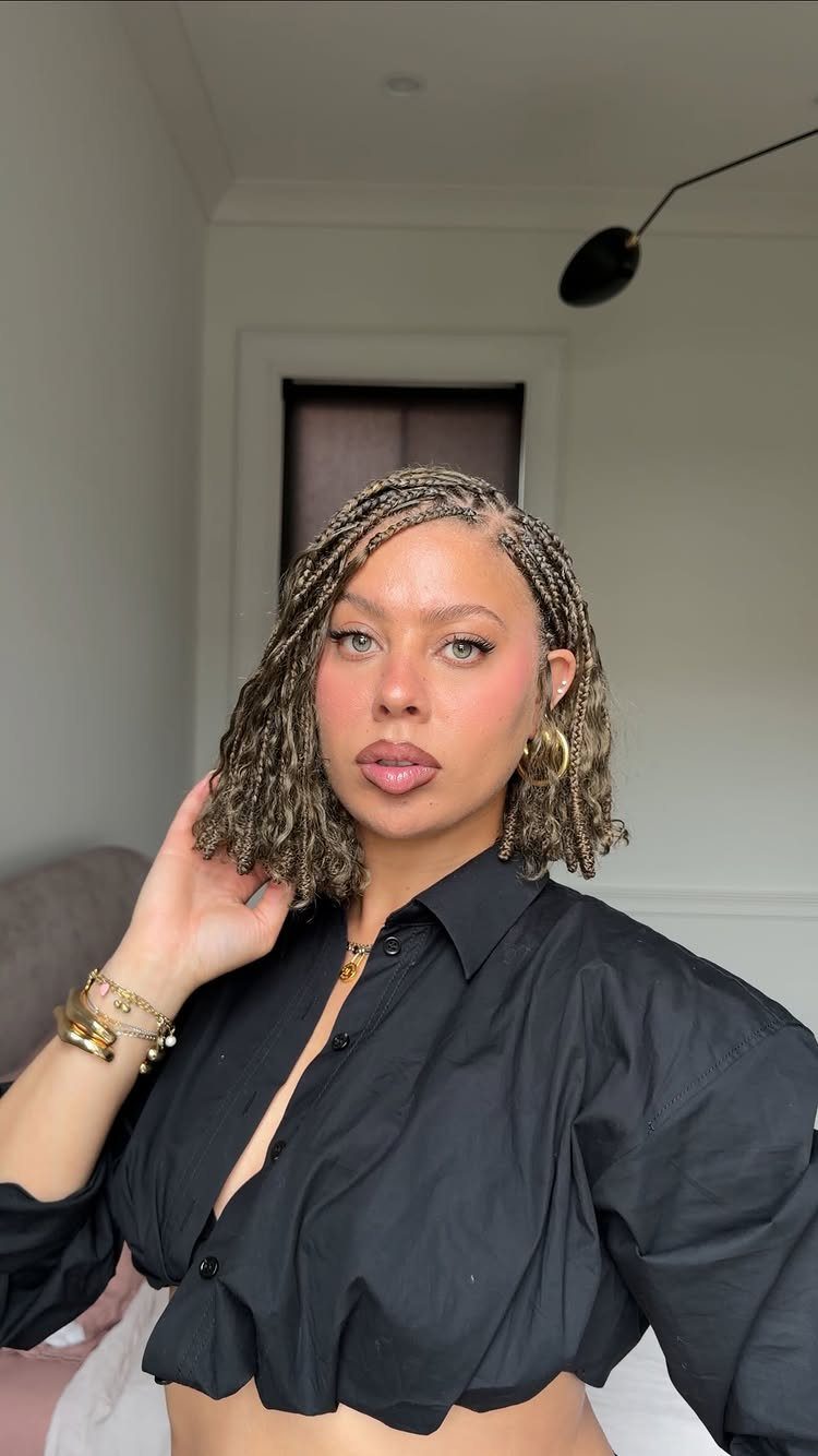 Woman with shoulder-length thin braids poses in a black cropped blouse