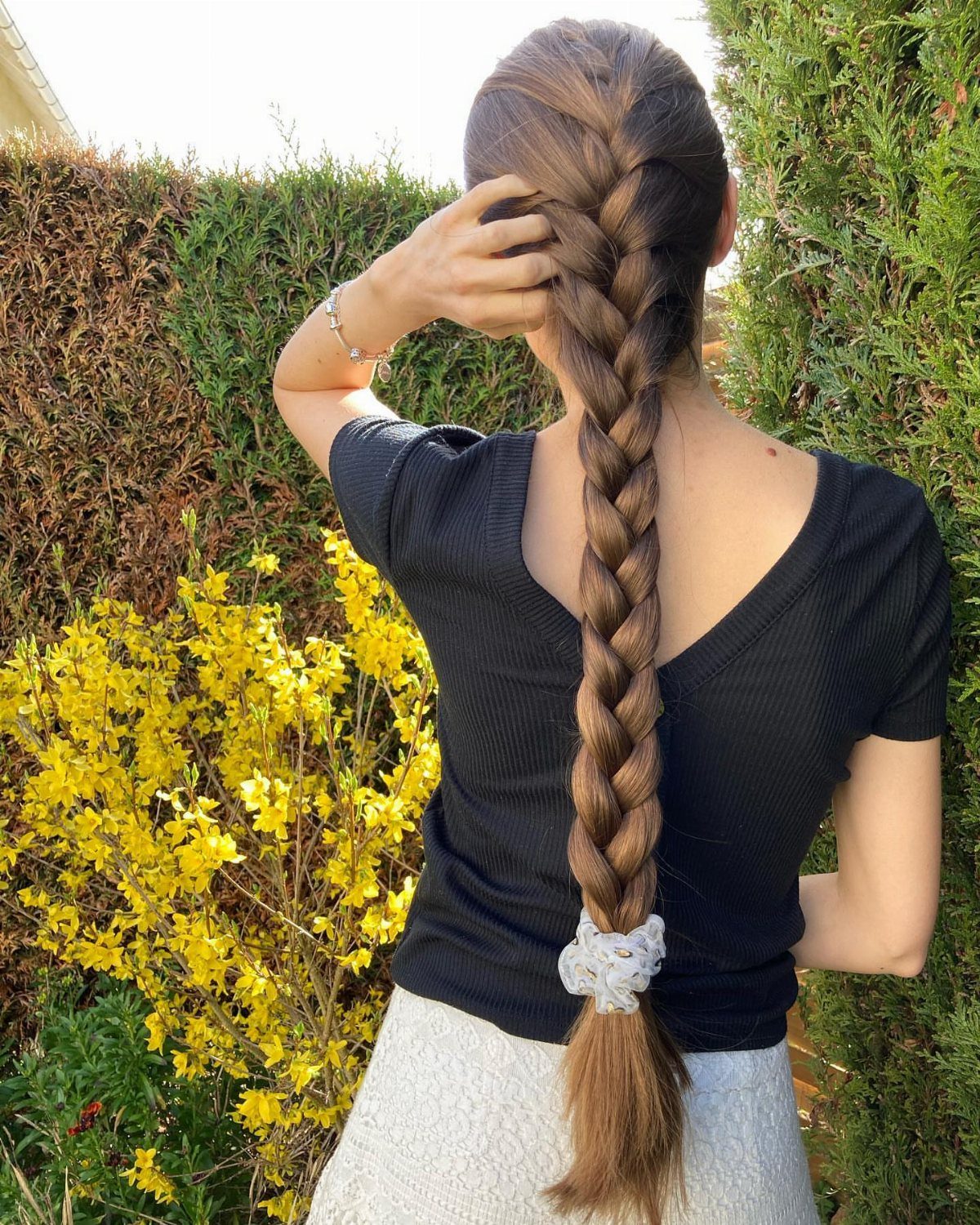 Long brown French braid secured with a white scrunchie outdoors