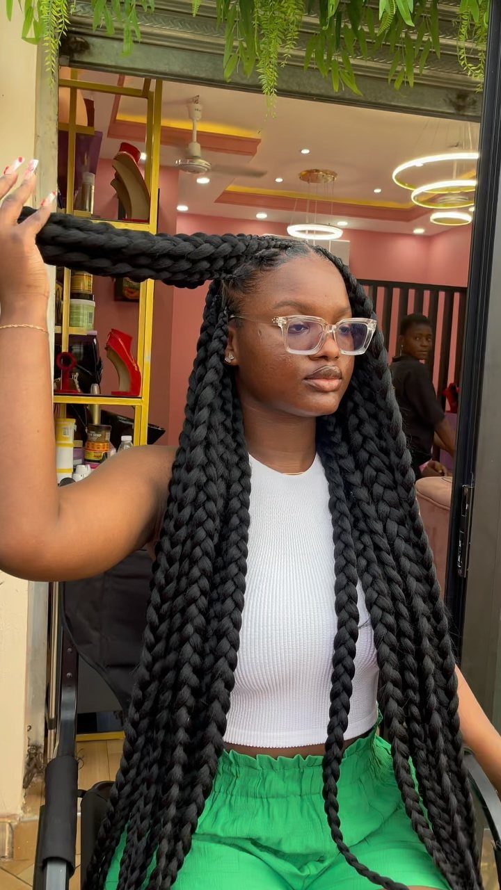 Woman with long, thick black box braids stands in a brightly lit salon