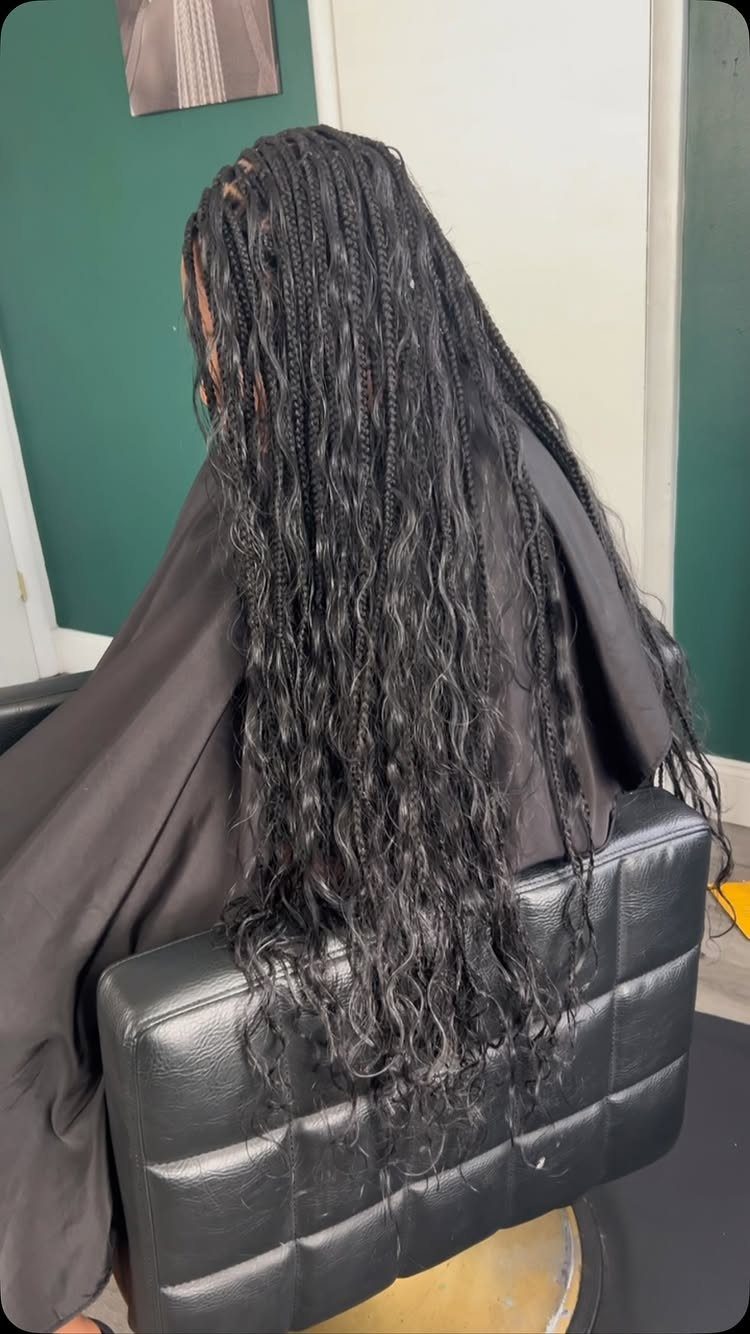 Long thin dark braids hang down the back over a black salon cape