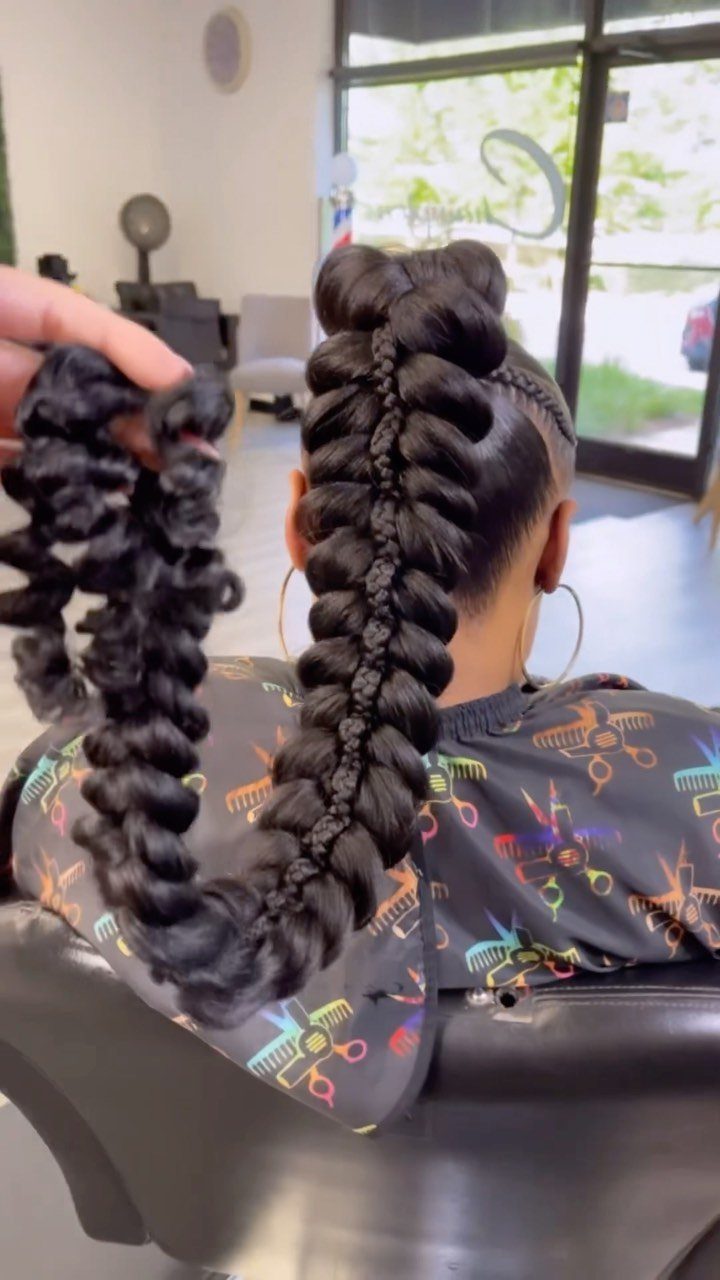 Thick black braided ponytail with a curly extension held beside it in a salon