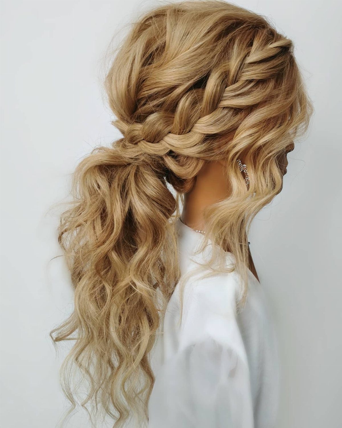 Blonde braided hair gathered into a low ponytail with long curls hanging loose