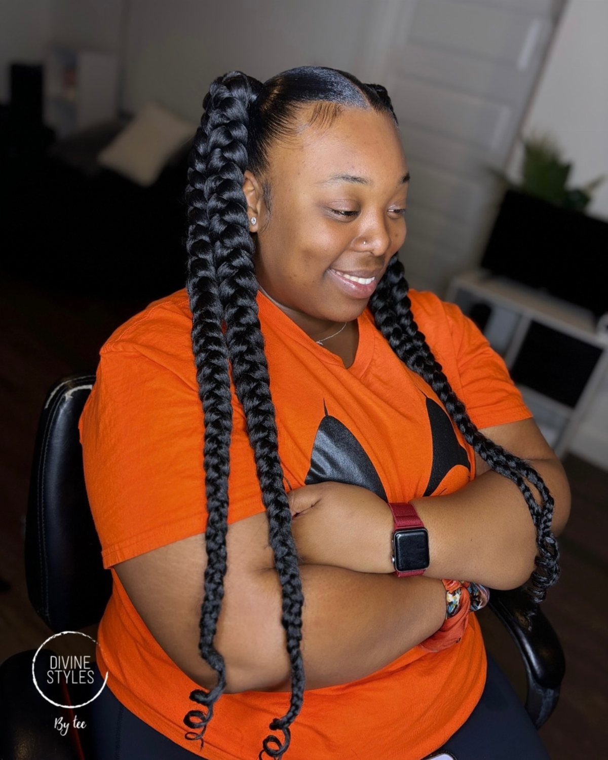 Woman showing two long black braided ponytails while seated indoors