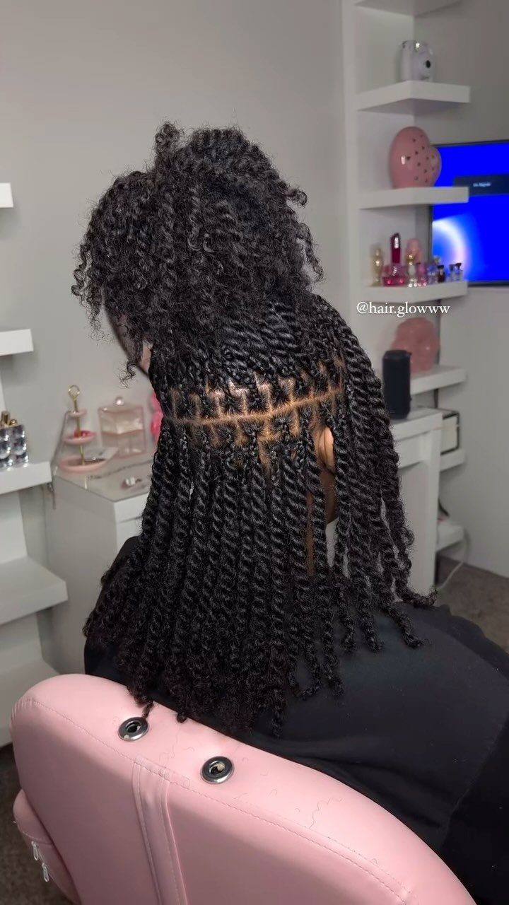 Long twists flow from a high curly puff in a salon chair