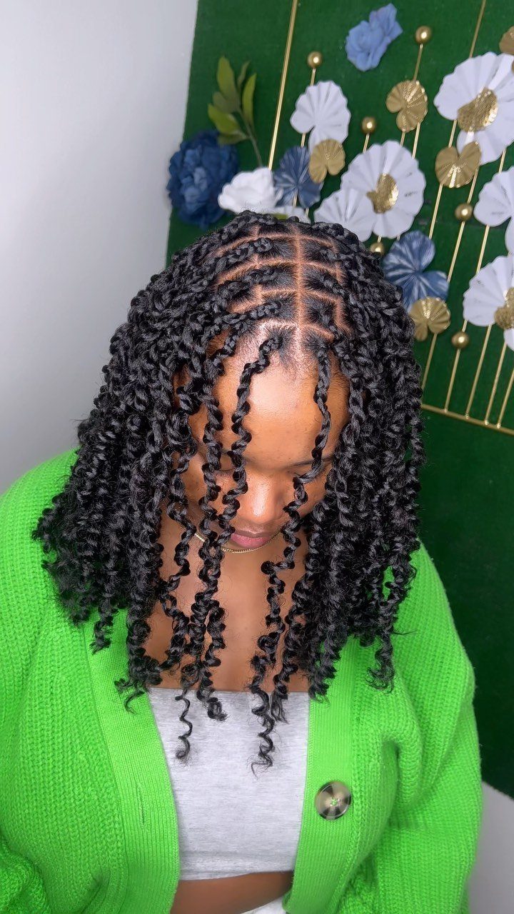 Woman with short black passion twists wears a bright green cardigan against a floral backdrop.