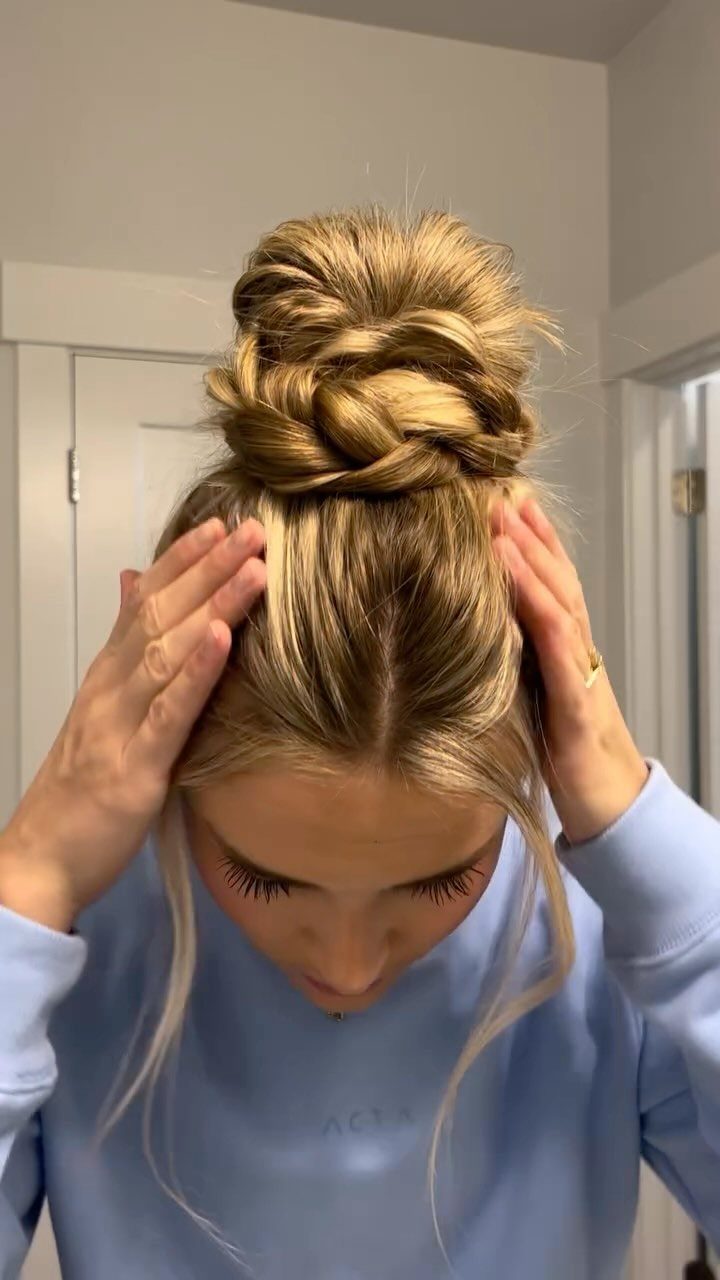 Loosely woven blonde braids form a large messy bun at the back of a woman's head