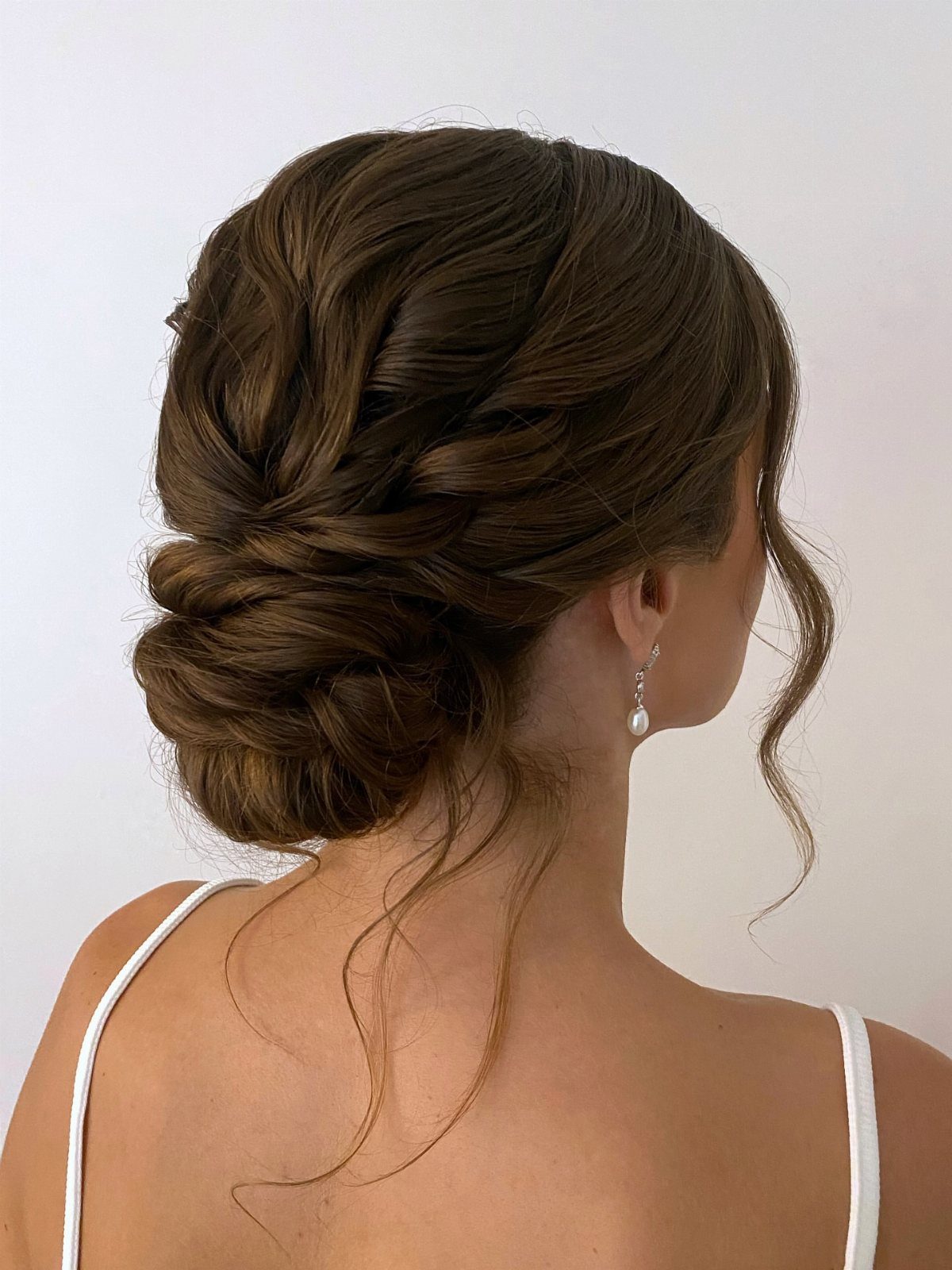 Low bun formed from thick twisted hair sections, with loose tendrils and a pearl earring