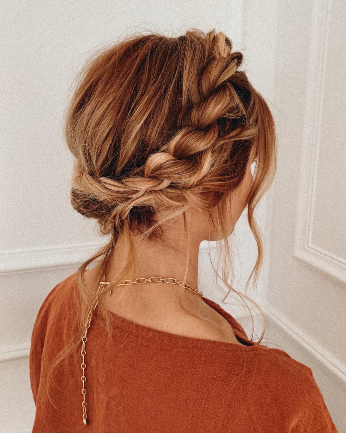 Low auburn bun formed from thick rope braids woven across the back of the head