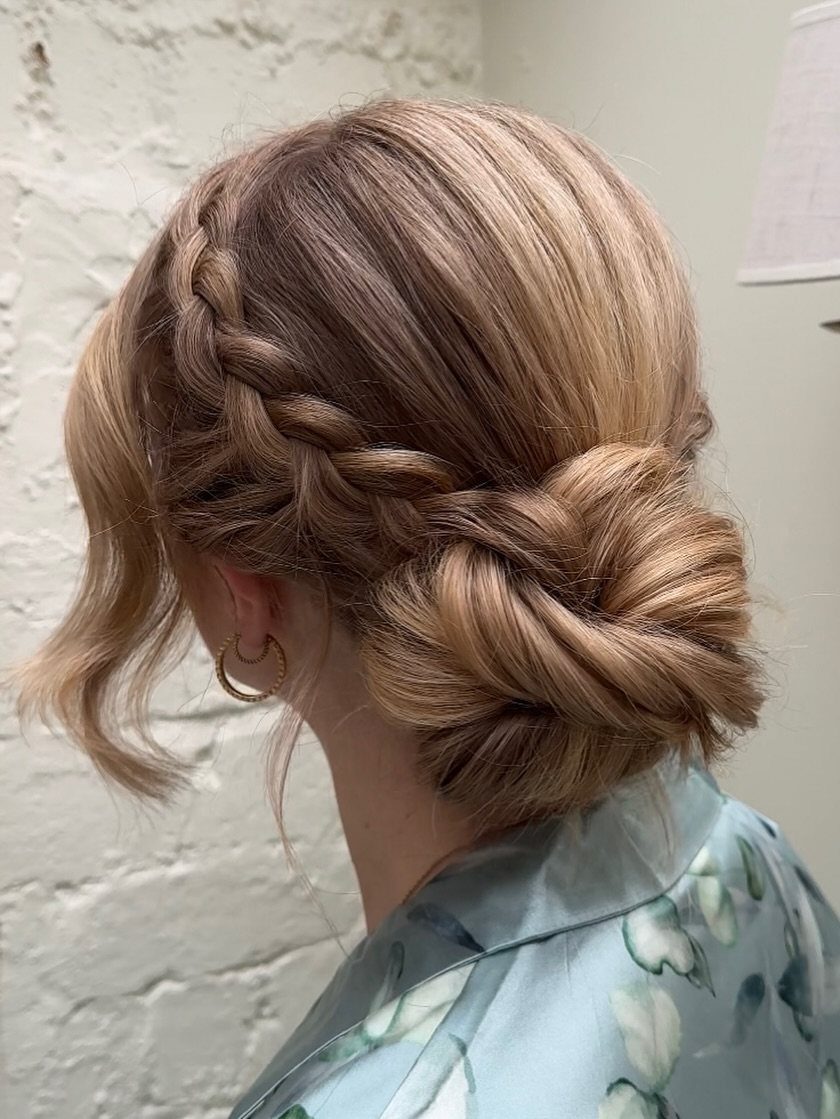 Loose low chignon with a side braid woven across softly waved brown hair