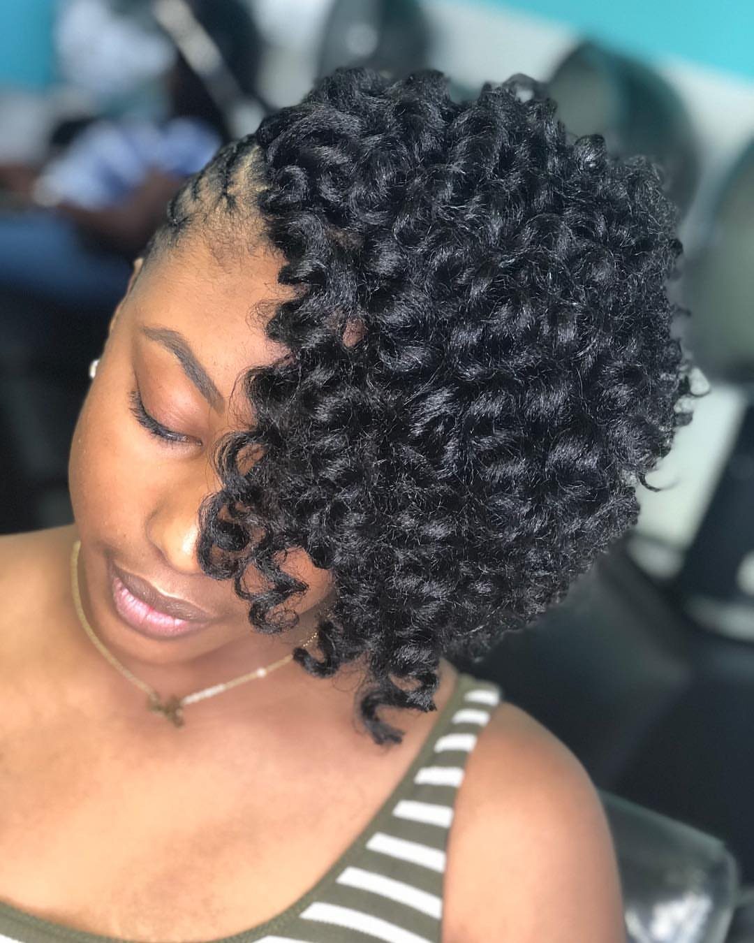 Woman showing short, dense black crochet curls against a dark indoor background
