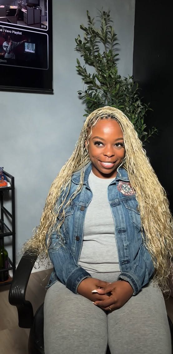 Woman with long pale blonde braids seated in a denim jacket