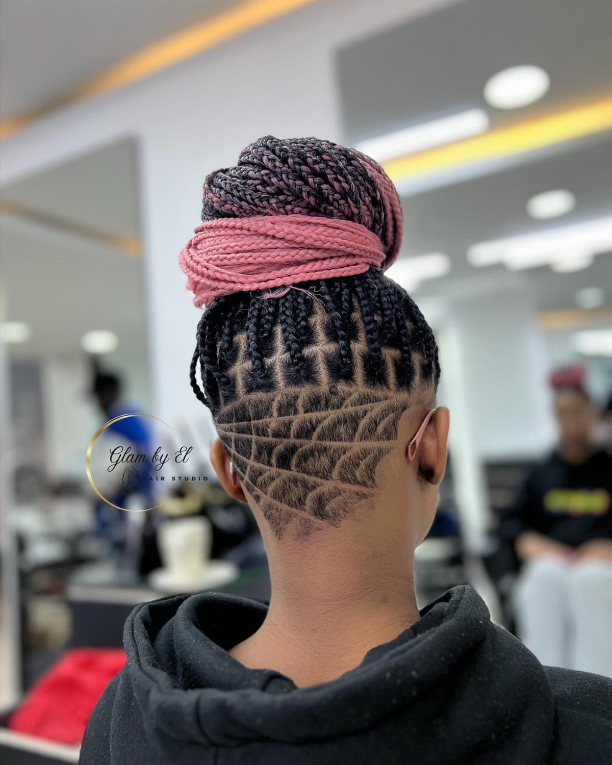 Cornrowed hair with a geometric undercut and a high pink-wrapped braided bun