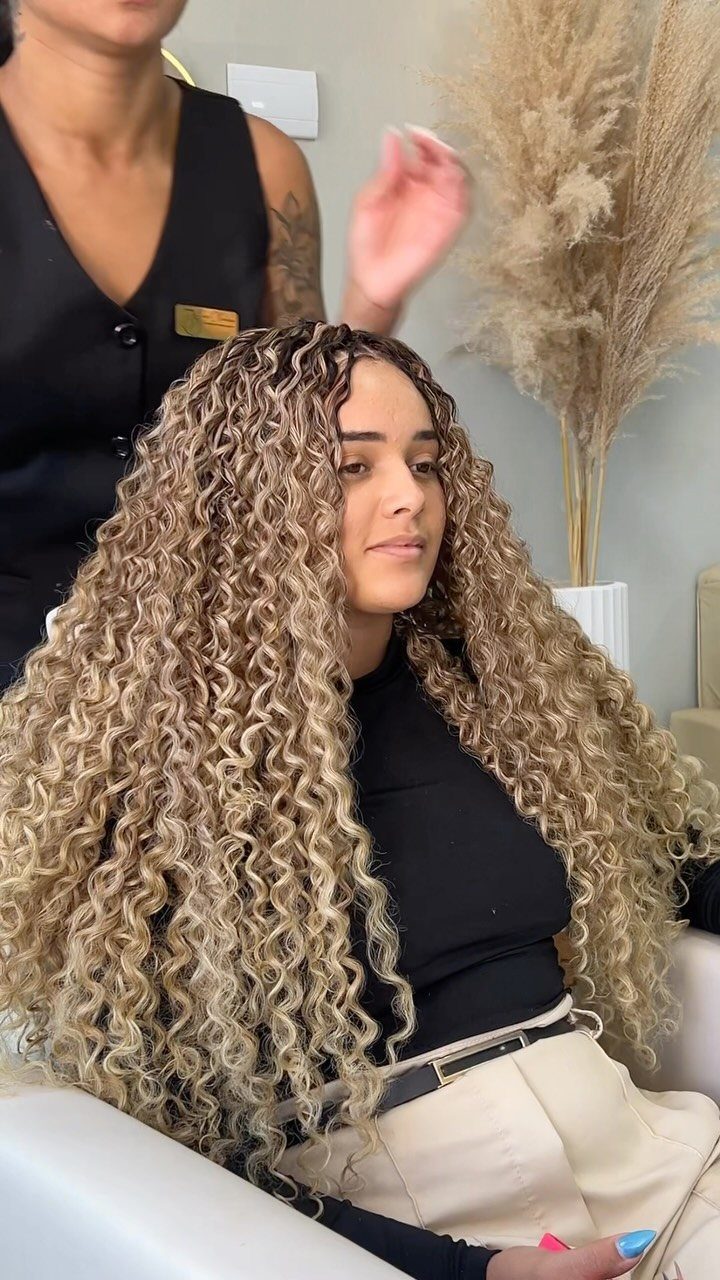 Woman displays long, voluminous wavy crochet braids in a salon
