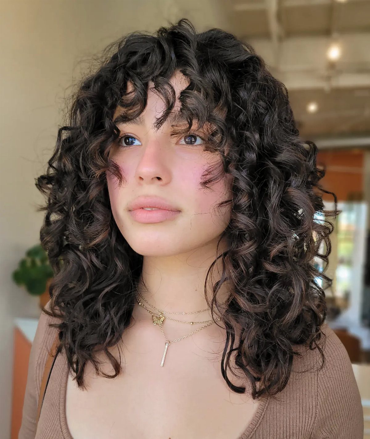 Person with long layered curls and defined bangs framing the forehead and face