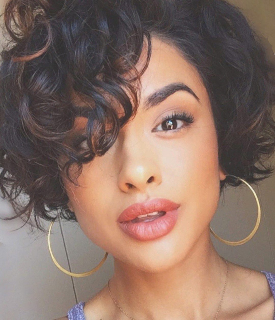 Woman with voluminous dark curls swept into side bangs framing her face