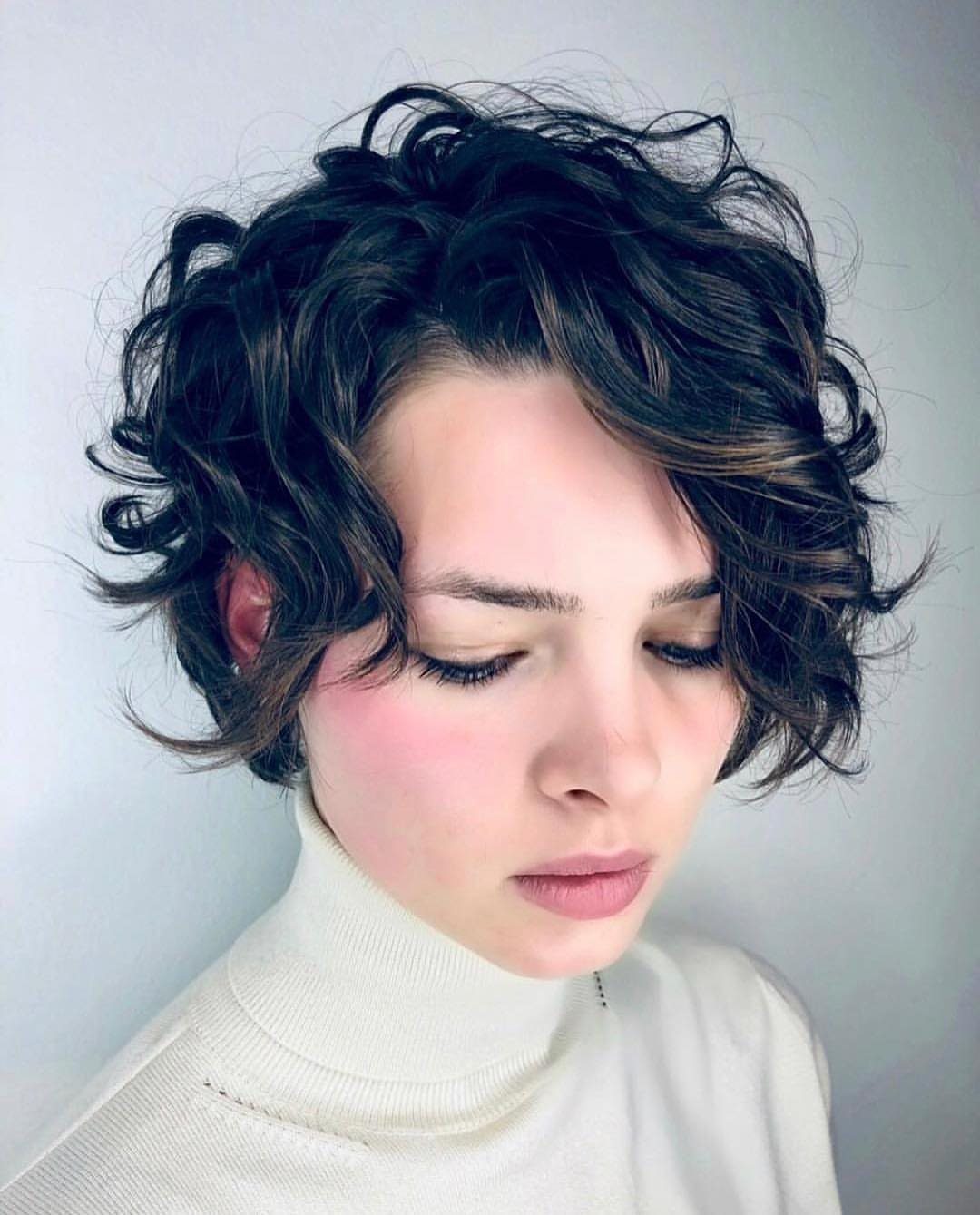 Person with short dark curly pixie cut, voluminous textured top, and shorter sides