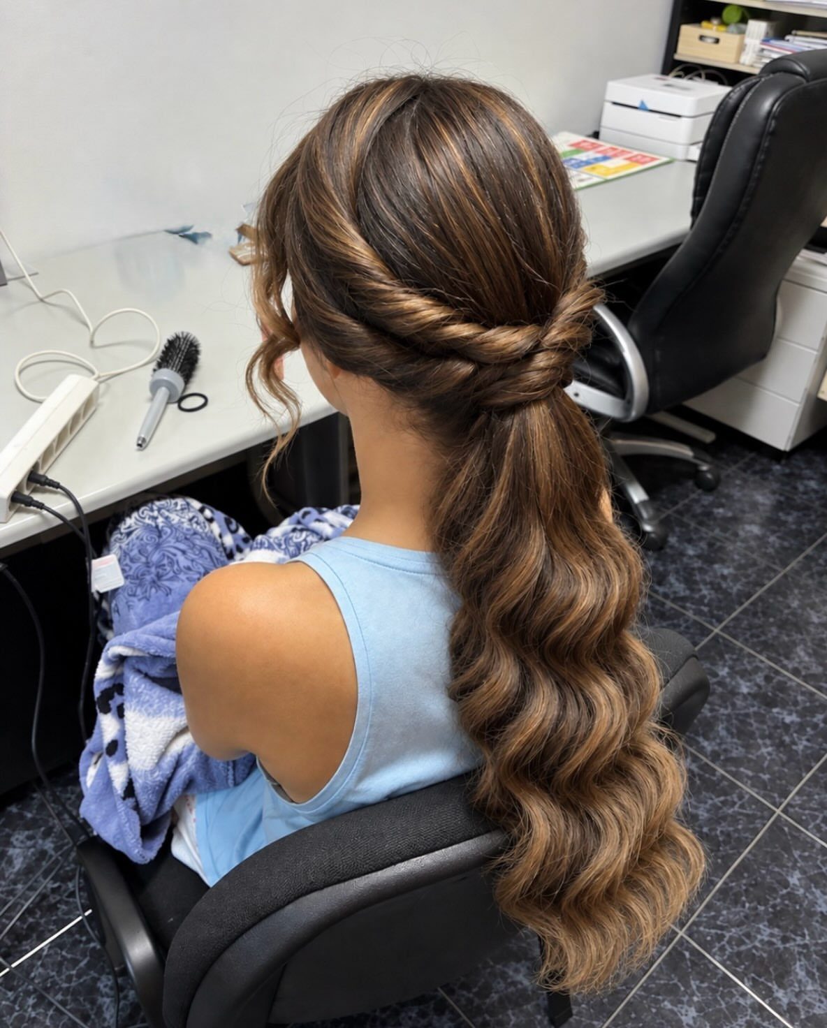 Low braided ponytail with long loose curls down a seated woman's back