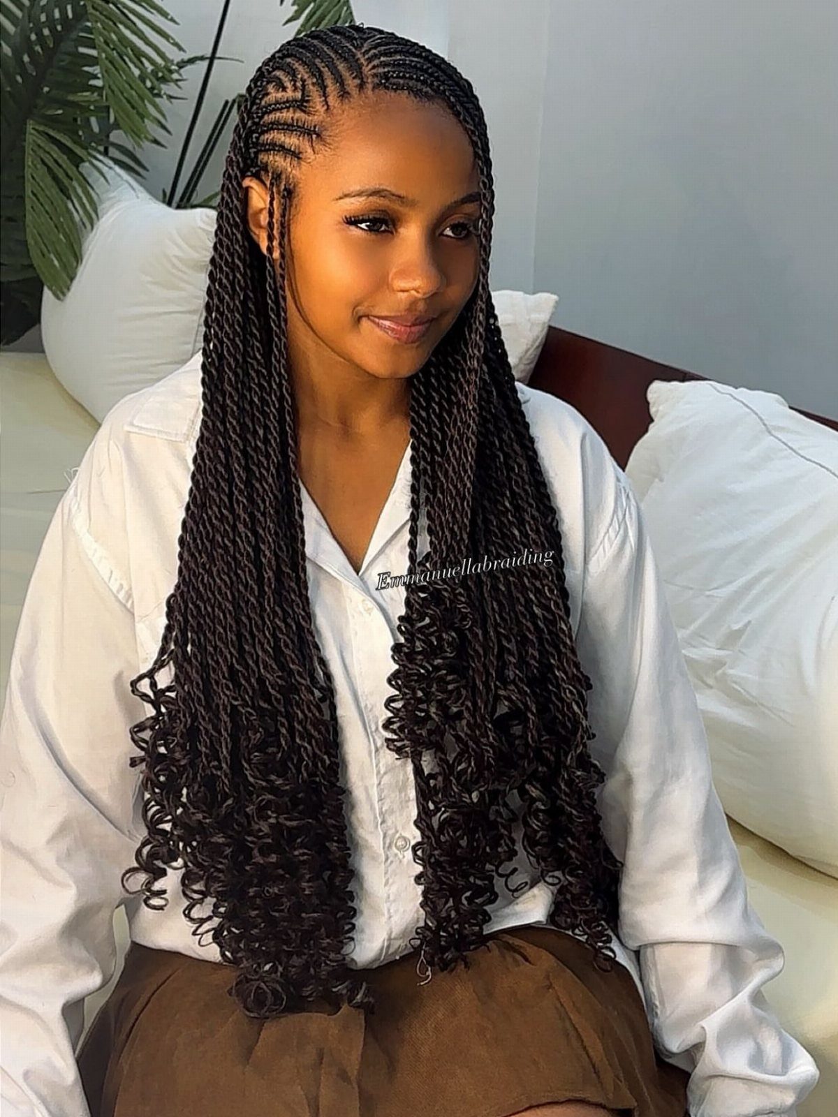 Woman with long dark braids ending in curls, seated on a bed