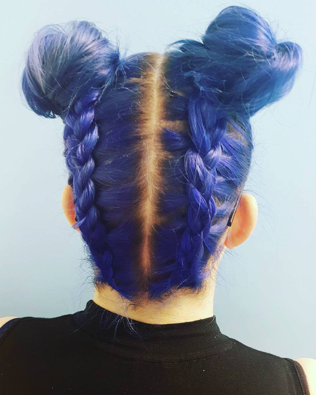 Blue Dutch braids gathered into two high buns on a person’s head