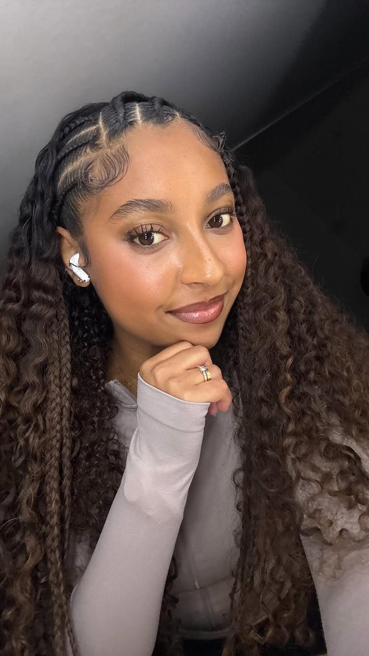 Woman with patterned cornrows and long curly braids posing indoors